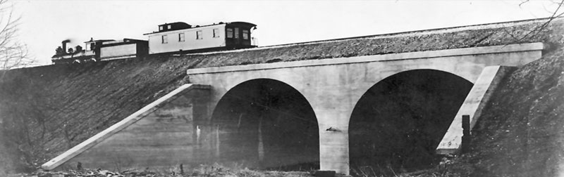 Atchison, Topeka and Santa Fe engine, coal car and caboose steaming over double arch style railroad bridge between Wellsville and LeLoup, 1910.